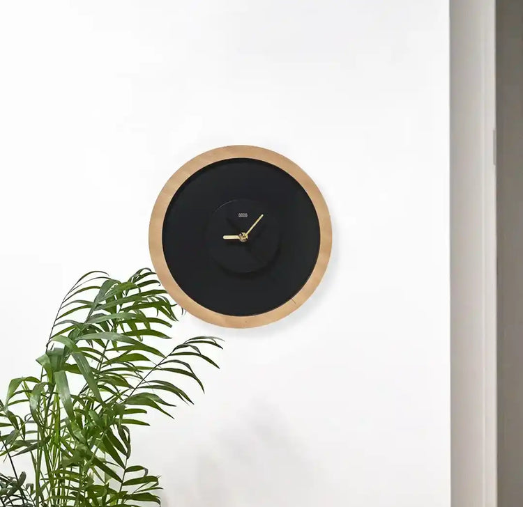 horloge en bois accrochée au mur avec un plante verte en avant plan
