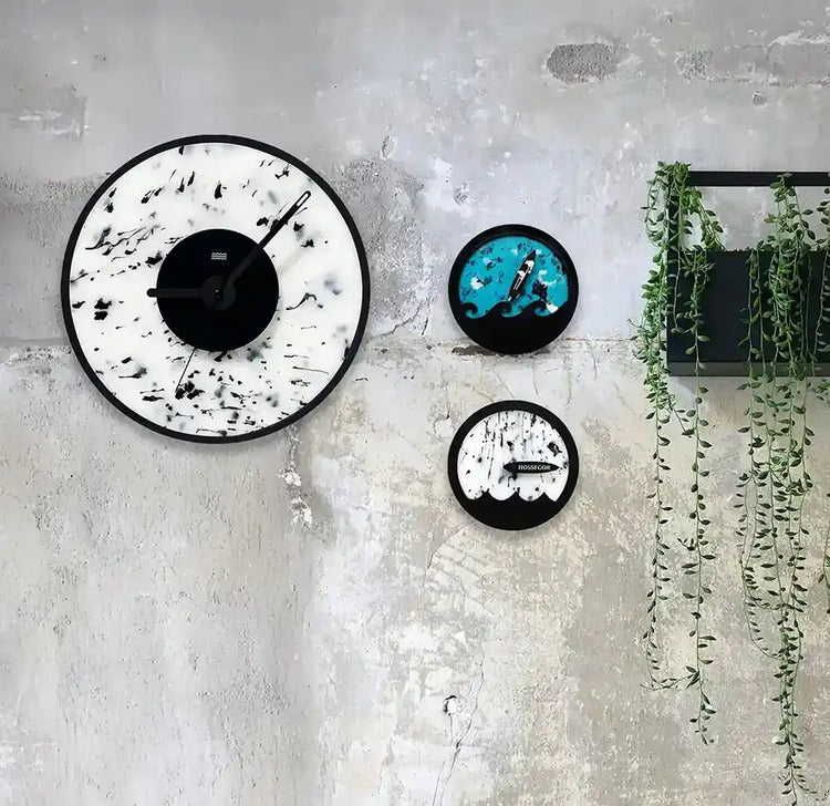 une horloge blanche et noire, une horloge des marées bleu et une horloge des marées blanche accrochées à un mur de beton