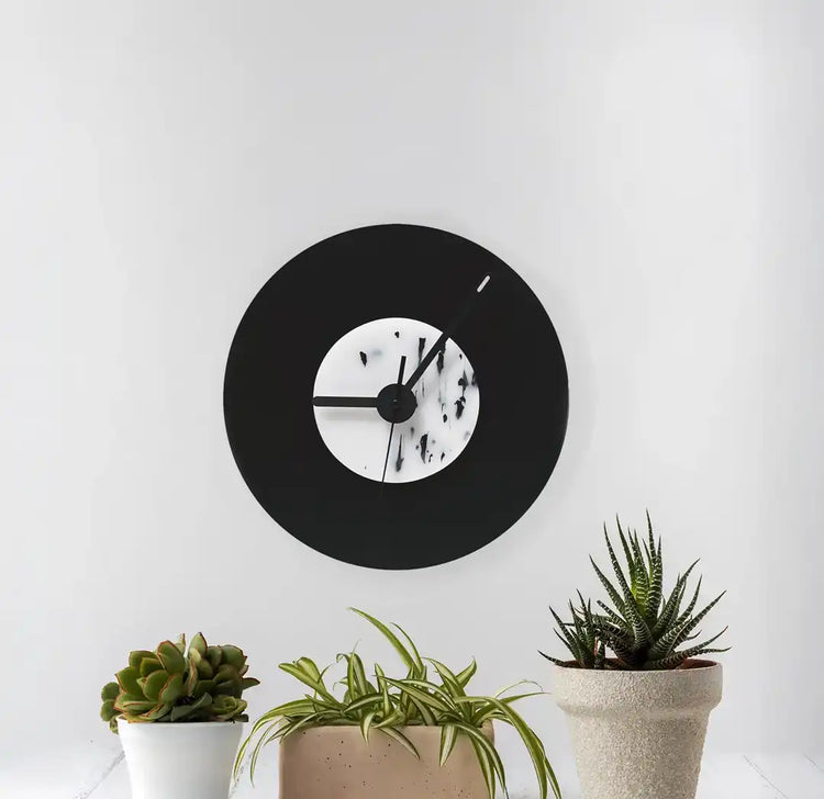 Horloge noir et blanche tachetée accrochée au mur devant 3 petits pots de fleurs