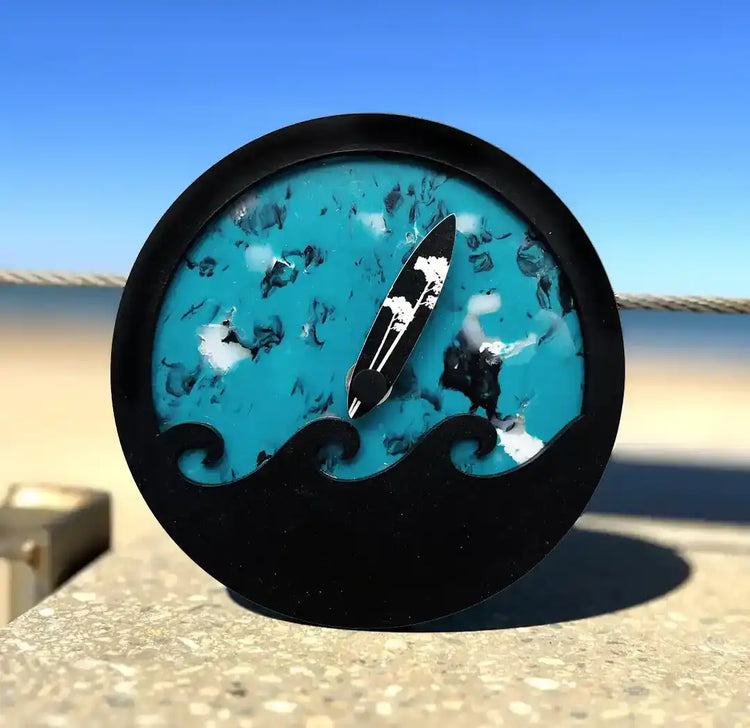 Horloge des marées bleu avec une vague noir en surimpression. Une aiguille en forme de planche de surf indique la marée