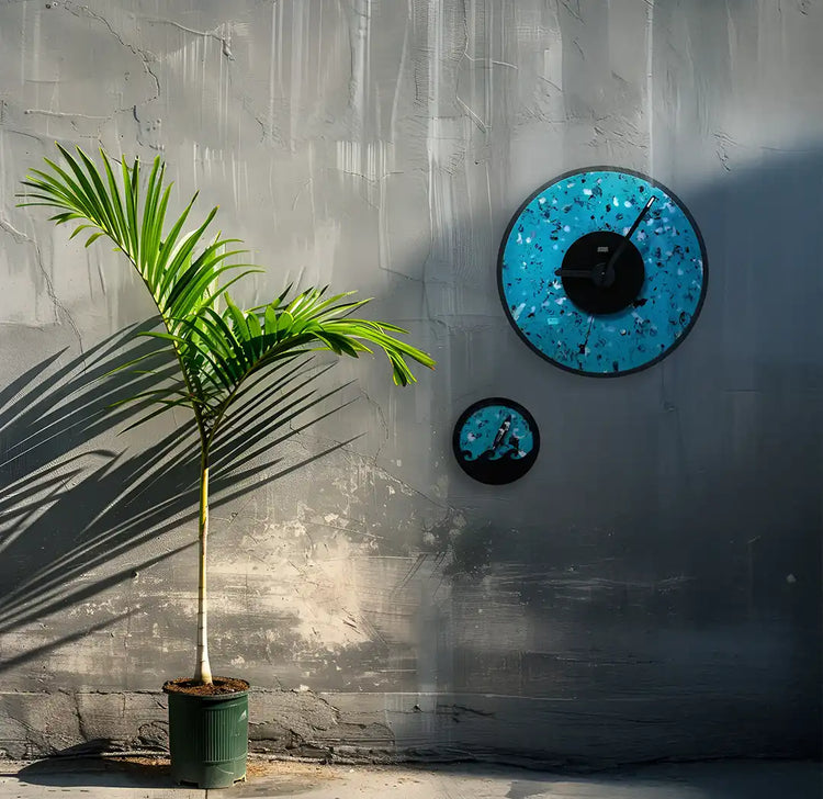 une horloge bleu et noire et une horloge des marées bleu et noir  accrochée au mur à côté d'un petit palmier en pot