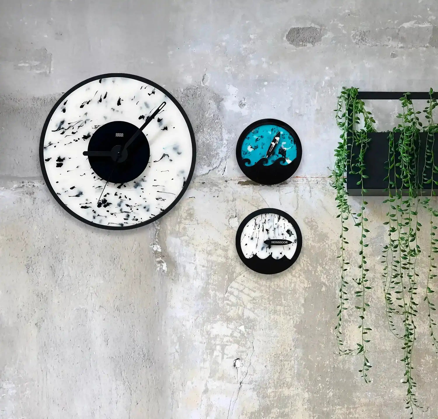 une horloge blanche et noire, une horloge des marées bleu et une horloge des marées blanche accrochées à un mur de beton